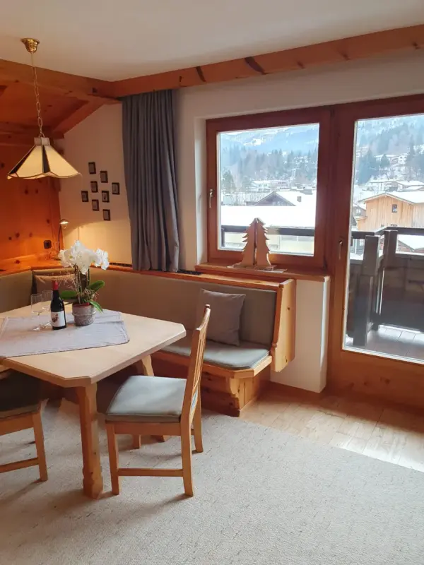 Blick vom Essbereich durch die große Balkontür auf die Holzhäuser der Nachbarschaft und die Berge. Die helle Eckbank lädt zum Verweilen ein.