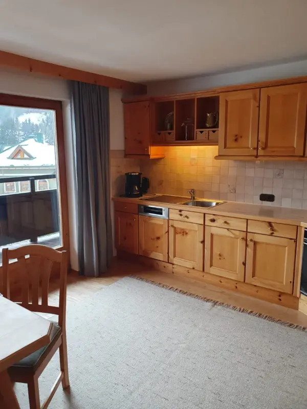 60m² Ferienwohnung: Rechts die rustikale Küchenzeile, links der lichtdurchflutete Essbereich mit Teppich und Zugang zum Balkon.