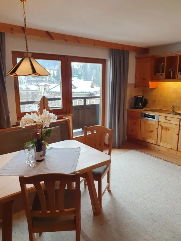 Helle, offene Wohnküche in Rosas Ferienwohnung. Zu sehen ist die hölzerne Küchenzeile, der Essbereich mit Hängelampe und die große Glastür zum Südbalkon.