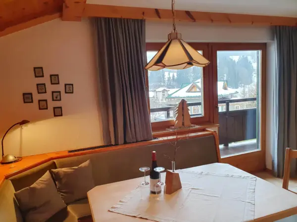 Rustikale Eckbank in einer Ferienwohnung mit Blick aus dem Fenster auf die verschneite Landschaft von Fieberbrunn.