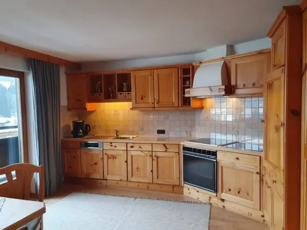 Große, helle Wohnküche im Holz-Design mit Spülmaschine, Kaffeemaschine und Zugang zum Balkon.