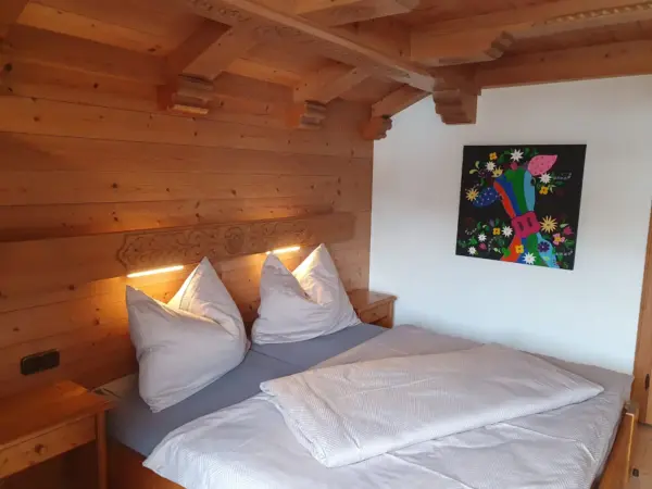 Rustikales Schlafzimmer mit Holzwänden und einem farbenfrohen, modernen Gemälde einer Kuh an der Wand neben dem Bett.