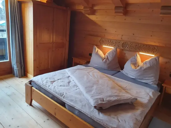 Ein massives Doppelbett aus Holz in einem vollverkleideten Holzzimmer mit warmen Leselampen und hellem Dielenboden.